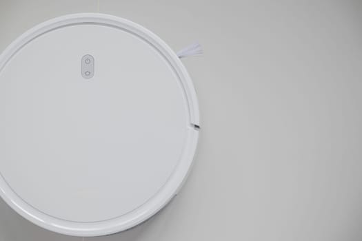 White automatic floor cleaner with side brush on tile flooring. Top view of robot vacuum cleaner removing dust, showcasing modern smart home cleaning technology for spotless and efficient maintenance