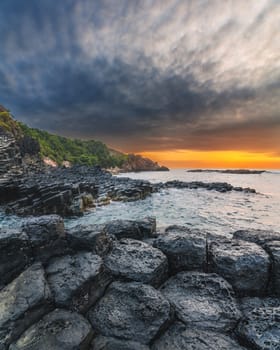 Landscape with black volcanic basalt columns on rocky beach by the sea. Da Da reef in Phu Yen province in Vietnam at sunrise