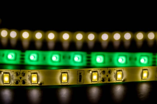 Three LED light strips glowing in green, yellow, and white tones against a dark background. Technology concept for lighting and electronics.
