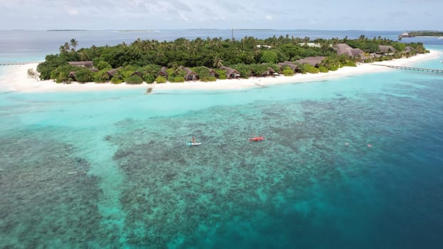 Tourists enjoying kayaking and paddleboarding in the crystal-clear turquoise waters of a tropical island resort in the maldives, highlighting the indian ocean's beauty