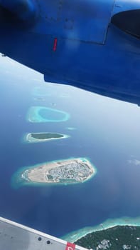 The wing of a seaplane offers a stunning perspective of the maldivian archipelago, showcasing the turquoise waters and lush greenery of these tropical islands