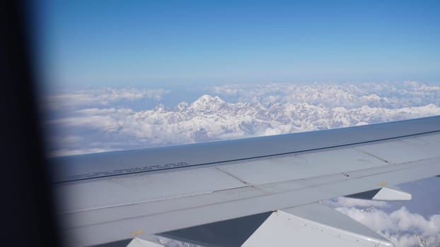 Airplane wing soaring above the snow-covered peaks of the majestic himalayas, with a clear blue sky stretching endlessly in the background, creating a breathtaking aerial view