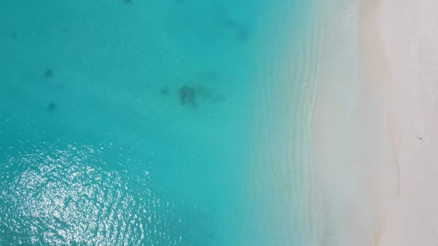 Aerial view of a beautiful tropical beach with crystal clear turquoise water gently lapping against the pristine white sand, creating a serene and idyllic scene, perfect for a relaxing getaway