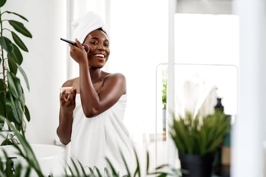 A woman enjoys her skincare routine, applying a facial mask and smiling in a well-lit bathroom decorated with lush green plants. The atmosphere is relaxing and inviting.