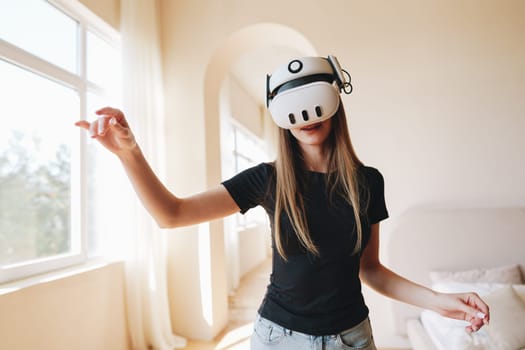 A young woman is immersed in a virtual reality experience in her cozy living room. She wears a VR headset and gestures with her hands, exploring a digital world.