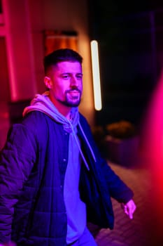 A young man strolls through a lively urban environment at night, surrounded by vibrant neon lights and a colorful atmosphere that enhances the nightlife experience.