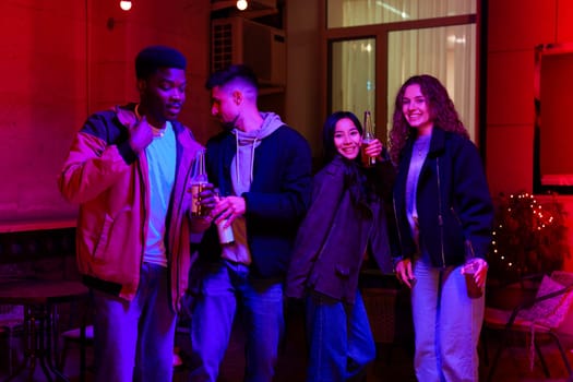 Four friends gather in a vibrant setting, laughing and sharing drinks. The warm glow of the lighting creates a cheerful atmosphere, perfect for socializing.