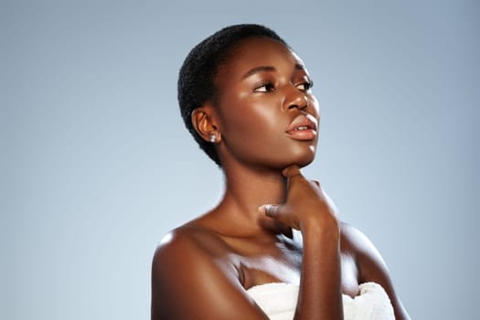 A woman with short hair strikes a contemplative pose, gently touching her chin. She is draped in a white towel, showcasing a natural and confident expression against a soft backdrop.