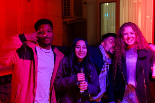 Four friends enjoy a lively evening together, displaying cheerful expressions while holding drinks. The space is filled with vibrant lighting, creating a joyful atmosphere.