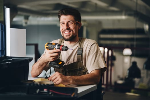 A skilled worker with a friendly smile holds a power drill in a modern workshop. Tools and materials are neatly arranged, showcasing a productive atmosphere.