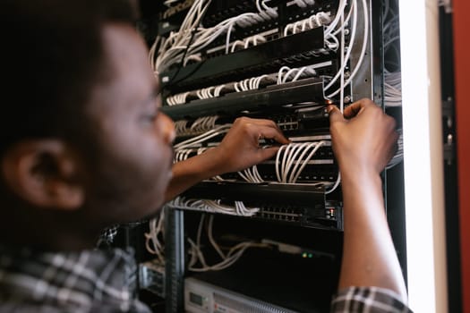 A technician is adjusting cables and securing connections on a server rack inside a data center. The environment is busy, with various network equipment visible.