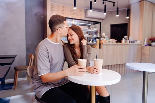 A young couple sits closely together at a small table in a cozy cafe, sharing smiles while sipping coffee. The relaxed atmosphere and warm lighting create a romantic vibe.