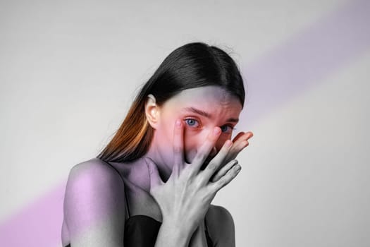 A model with long hair shows a vulnerable moment by covering her face with her hands, captured in artistic black and white with subtle color highlights.