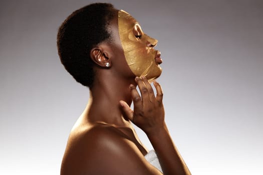A woman with short curly hair applies a gold facial mask while enjoying a self-care moment. The softly lit atmosphere enhances the tranquil vibe, promoting relaxation and rejuvenation.