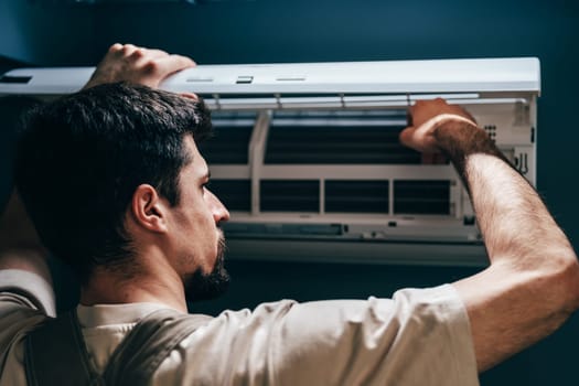 A technician works on a wall-mounted air conditioning unit in a contemporary room. He carefully adjusts the inner components to ensure optimal performance and efficiency.