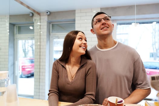 A couple shares joyful smiles while gazing at the cafe's interior. Sunlight filters through the windows, creating a warm atmosphere for their visit.