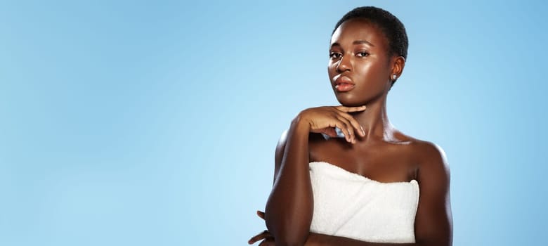 A model stands gracefully in front of a light blue backdrop, exuding confidence. Wearing a white towel and displaying a serene expression, she highlights her natural beauty and poise.