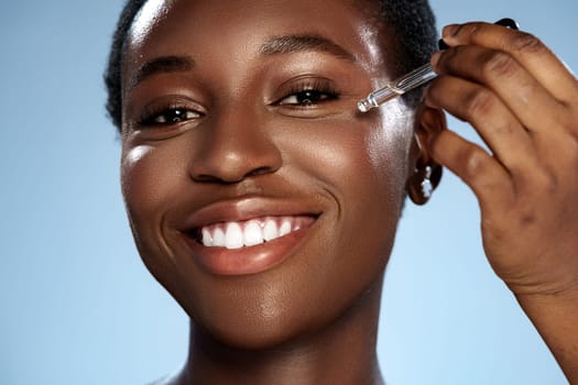 A smiling woman applies a serum to her cheek in a well-lit space, showcasing her healthy skin and enjoyment of self-care. The glow reflects her skincare dedication and positivity.