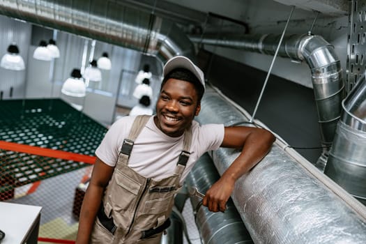 A young man with a cheerful expression leans casually against metal piping in a modern workspace.