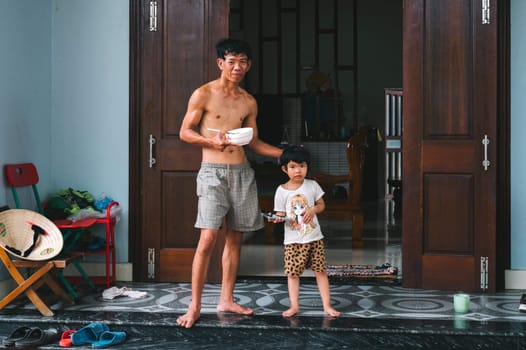 Asian family in the village. A Vietnamese dad with a child girl daughter are standing near house. Tam Tien, Quang Nam province, Vietnam - April 10, 2025