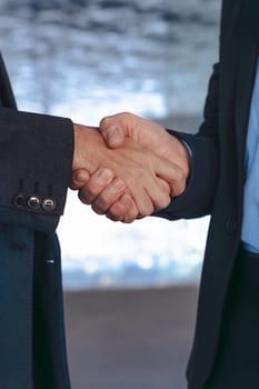 Vertical Portrait Two professional businessmen in suits shaking hands inside a modern glass office. Business deal, agreement, or partnership in a corporate indoor setting with contemporary design.
