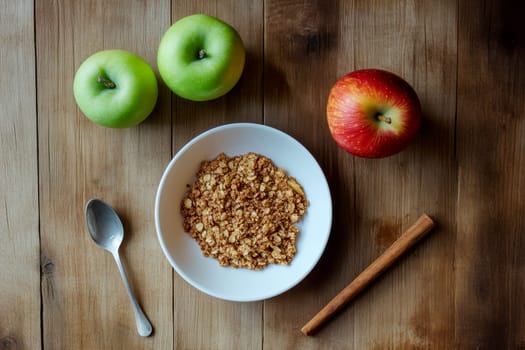 Apple crumble served on a white plate alongside a spoon and fresh green and red apples..