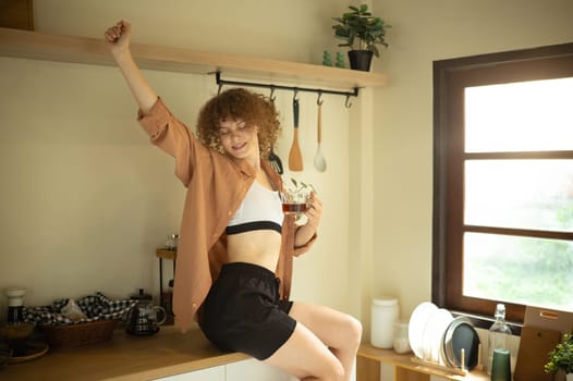 Home lifestyle scene of woman with curly hair enjoying a warm drink in her kitchen.