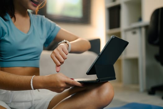 Young woman checking her smartwatch and following an online fitness session at home.