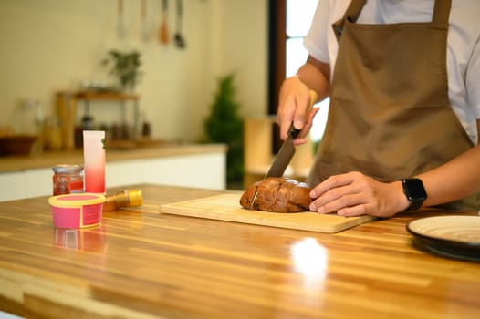 Man preparing breakfast by slicing loaf of bread, with ingredients arranged on a wooden countertop.