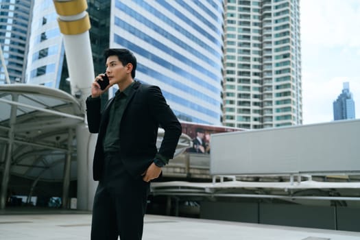 Businessman making a phone call outdoors with modern skyscrapers in the background.
