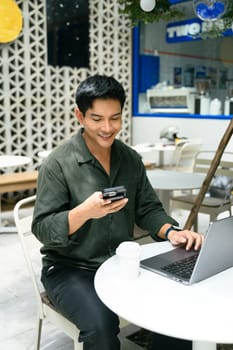 Smiling man checking his phone while working remotely on his laptop.