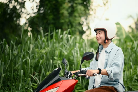 Happy asian man wearing a helmet scooter rider cruising through green countryside.