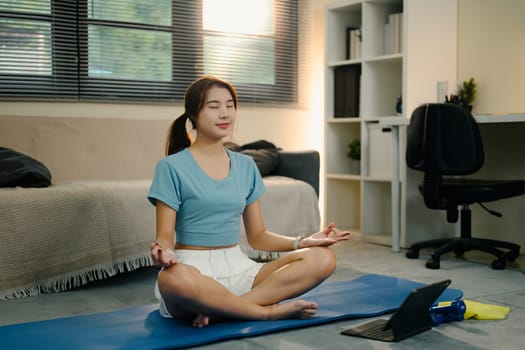 Asian woman practicing mindfulness and breathing exercises in a living room.