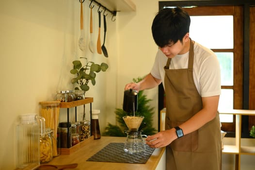 Asian man preparing a fresh cup of drip coffee in a modern, organized kitchen.