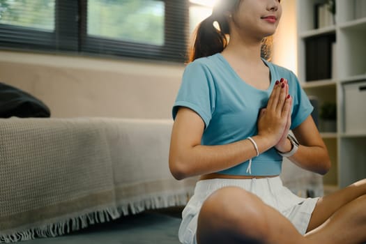 Asian woman in sportswear meditating in a cozy living room.