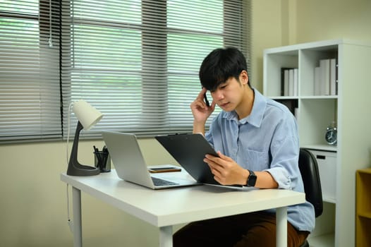 Focused freelancer reviewing documents at modern white desk with digital devices.