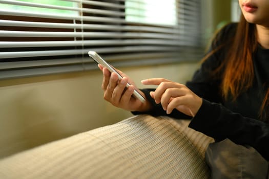 Close up of woman hands using smartphone on sofa at home.