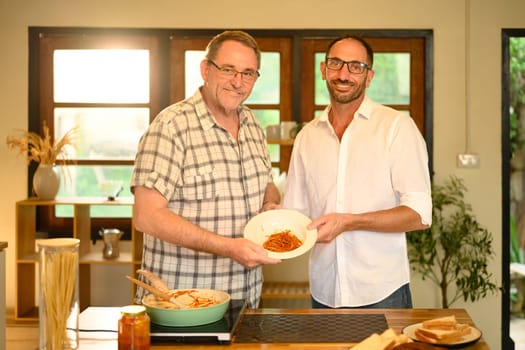 Elderly father and adult son presenting their finished meal in a warm home kitchen. Fathers day concept.