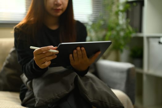 Cropped shot of female freelancer with stylus working on digital tablet at home.