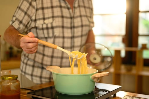 Close up of mature man preparing spaghetti in a cozy kitchen.