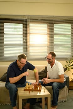 Father and adult son enjoying a game of chess in cozy living room. Fathers day concept..