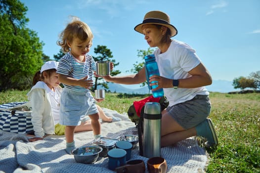 A mother and her children enjoy a sunny picnic amidst scenic nature, celebrating outdoor bonding and family relationships in a serene mountain setting.