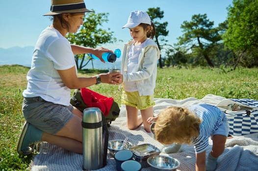 Family time outdoors during a picnic on a radiant summer day in the mountains. A parent and children share a bonding moment amid a picturesque natural setting, featuring clear skies and greenery.