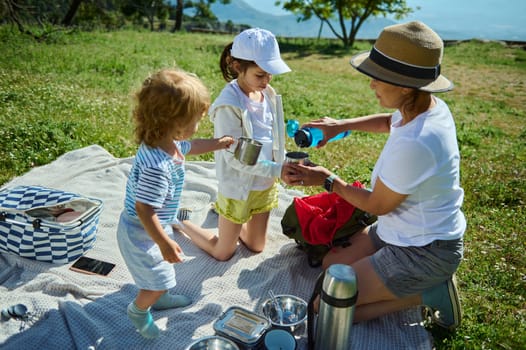 A mother enjoying National Picnic Month with her kids outdoors on a warm day, depicting familial bonding, nature appreciation, and outdoor leisure, with a focus on happy family moments.