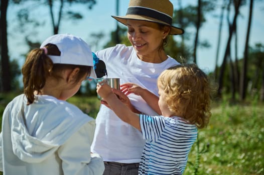 A mother spends quality time with her children outdoors during a nature picnic, enjoying sunshine and bonding amidst picturesque scenic mountain surroundings.