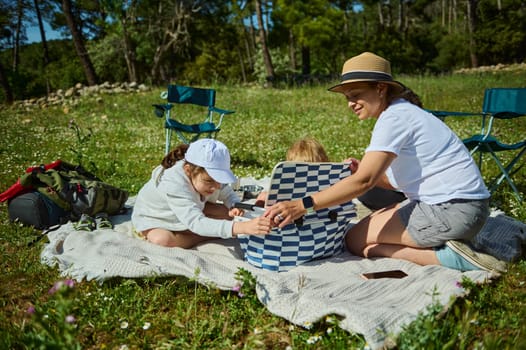 A mother and her children share a joyful picnic in a serene mountain meadow, enjoying the sunny outdoors and strengthening family bonds.