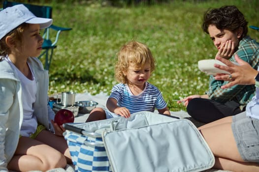A cheerful scene of a family enjoying an outdoor picnic in a natural setting. Parents and children share quality time during a sunny day in the mountains.