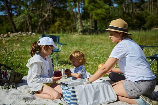 A mother and her children share a delightful picnic outdoors in lush nature, enjoying sunny weather and family bonding time. The vibrant scene highlights joy, tranquility, and memorable moments.