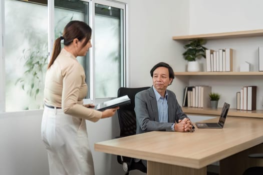A businesswoman hands over documents to a businessman during a meeting, showcasing teamwork and professional collaboration in a modern workspace.