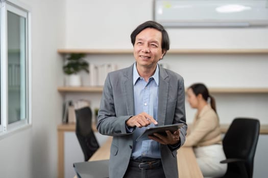 A businessman interacts with a tablet, smiling in a modern office setting, showcasing a positive work environment.